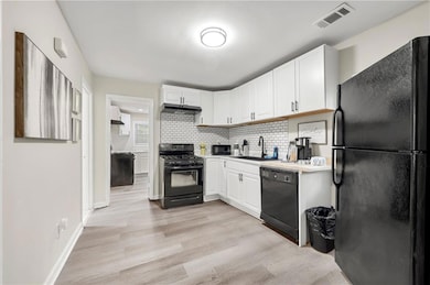 Kitchen with black appliances, a sink, white cabinets, and light wood finished floors