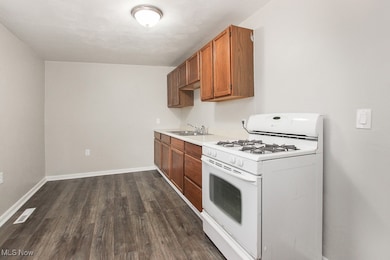 Kitchen with white gas range oven, light countertops, dark wood-type flooring, and brown cabinetry