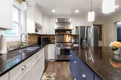 Kitchen with stainless steel appliances, wall chimney exhaust hood, white cabinets, open shelves, and pendant lighting
