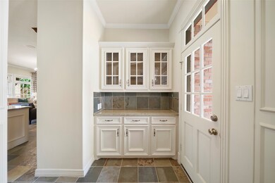 Tucked away behind the formal dining room with convenient access to the kitchen, the butler's pantry with slate tile flooring and a glass door leading to the driveway and 3-car garage features upper glass display cabinets with a granite surfaced serving counter with a slate tiled back splash and drawer & cabinet storage below.