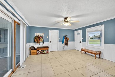Foyer entrance with a textured ceiling, ornamental molding, light tile patterned floors, ceiling fan, and a wainscoted wall