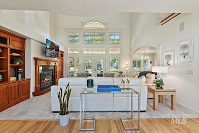Living area with wood finished floors, a glass covered fireplace, a high ceiling, a chandelier, and french doors