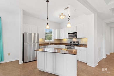 Kitchen with appliances with stainless steel finishes, dark stone countertops, hanging light fixtures, tasteful backsplash, and white cabinets