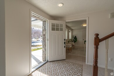 Entrance foyer with light tile patterned floors, a textured ceiling, stairs, and baseboards