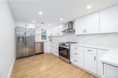 Kitchen with appliances with stainless steel finishes, white cabinetry, wall chimney range hood, wood finish floors, and recessed lighting