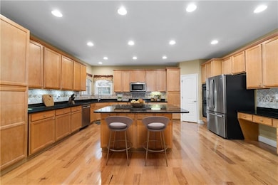 Kitchen with undermount counter lighting, double ovens, new bosch dishwasher, refrigerator w/ice maker!stainless steel finishes, backsplash, a center island, a breakfast bar, and light wood-type flooring