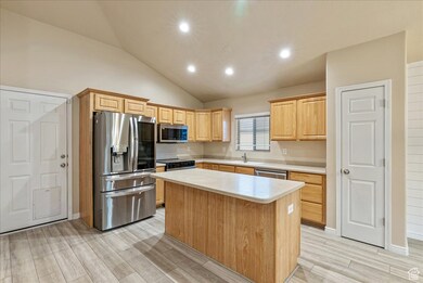 Kitchen with light brown cabinets, appliances with stainless steel finishes, a kitchen island, recessed lighting, and lofted ceiling