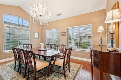 Dining space with wood-type flooring, healthy amount of natural light, lofted ceiling, and a chandelier