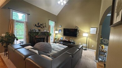Living room featuring a ceiling fan, baseboards, high vaulted ceiling, a fireplace, and light carpet