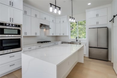 Kitchen featuring appliances with stainless steel finishes, a center island, hanging light fixtures, a barn door, and light wood-style floors
