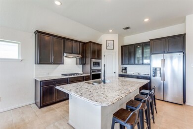 Kitchen with appliances with stainless steel finishes, dark brown cabinets, tasteful backsplash, light tile patterned flooring, and lofted ceiling
