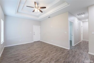 Empty room featuring a tray ceiling, a ceiling fan, and wood finished floors