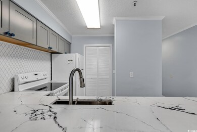 Kitchen featuring white appliances, gray cabinets, ornamental molding, light stone countertops, and a textured ceiling