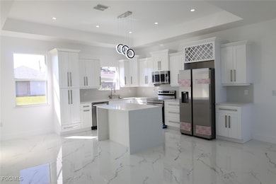 Kitchen featuring stainless steel appliances, a tray ceiling, a kitchen island, hanging light fixtures, and white cabinets