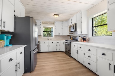 Kitchen with white cabinets, appliances with stainless steel finishes, light wood finished floors, decorative backsplash, and wooden ceiling