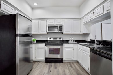 Kitchen with appliances with stainless steel finishes, white cabinets, light wood-type flooring, and dark stone counters