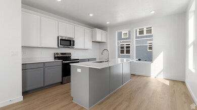 Kitchen with appliances with stainless steel finishes, gray cabinets, light wood-style floors, a center island with sink, and recessed lighting