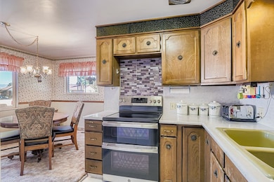 Kitchen featuring double oven range, light countertops, a chandelier, brown cabinetry, and wallpapered walls