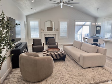 Living area with a textured ceiling, vaulted ceiling, a glass covered fireplace, a ceiling fan, and a chandelier