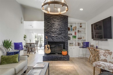 Living room with light wood-style floors, lofted ceiling, a fireplace, a chandelier, and recessed lighting