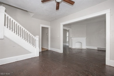 Unfurnished living room with dark wood-type flooring, stairs, a textured ceiling, a ceiling fan, and a premium fireplace