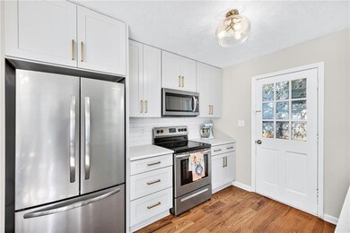 Kitchen featuring stainless steel appliances, white cabinetry, light wood finished floors, a textured ceiling, and backsplash