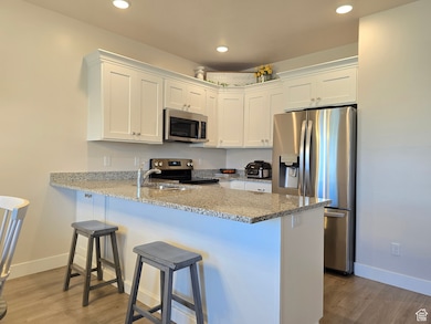 Kitchen featuring appliances with stainless steel finishes, light stone counters, white cabinetry, a peninsula, and dark wood finished floors