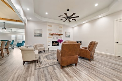 Living room with ceiling fan, a raised ceiling, light wood-type flooring, a large fireplace, and recessed lighting