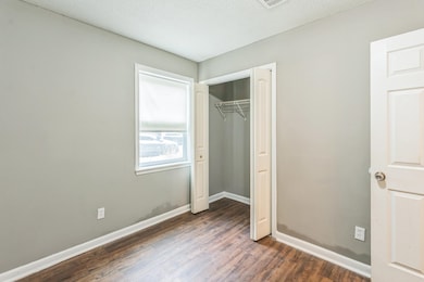 Unfurnished bedroom with dark wood-style flooring, a closet, and baseboards