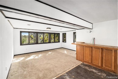 Unfurnished room with beam ceiling and dark colored carpet