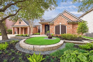 This is a single-story brick home with an arched entryway, gabled rooflines, and an inviting landscaped front yard featuring a circular garden bed and mature trees.