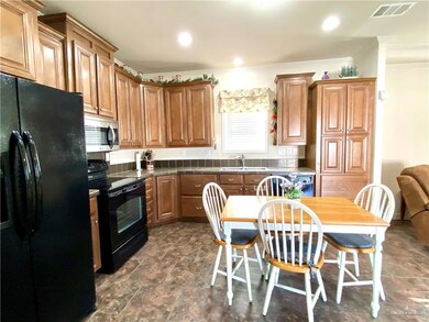 Kitchen featuring black appliances, brown cabinets, crown molding, recessed lighting, and stone finish floors