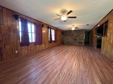 Unfurnished living room featuring dark wood-type flooring, wood walls, ceiling fan, and a textured ceiling