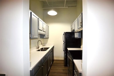 Kitchen with black appliances, a sink, light countertops, dark wood finished floors, and under cabinet range hood