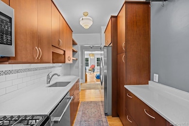 Kitchen featuring light wood finished floors, appliances with stainless steel finishes, light countertops, ornamental molding, and brown cabinetry