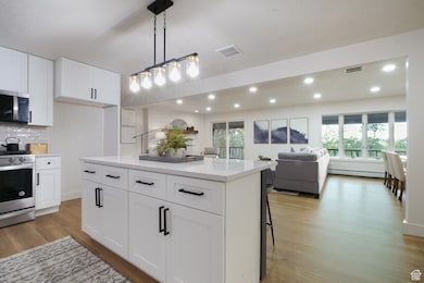 Kitchen featuring white cabinets, stainless steel appliances, pendant lighting, open floor plan, and a center island