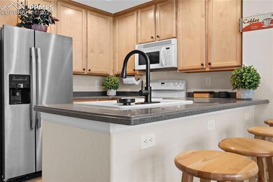 Kitchen featuring white appliances, a peninsula, a kitchen breakfast bar, and light brown cabinetry