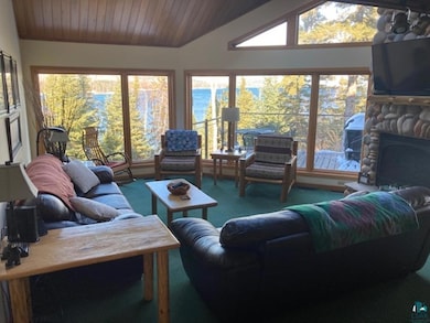Carpeted living area with wooden ceiling, vaulted ceiling, and a stone fireplace