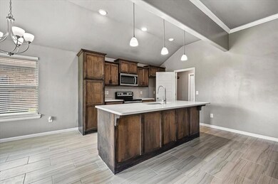 Kitchen featuring a chandelier, vaulted ceiling, stainless steel appliances, light countertops, and a kitchen island with sink
