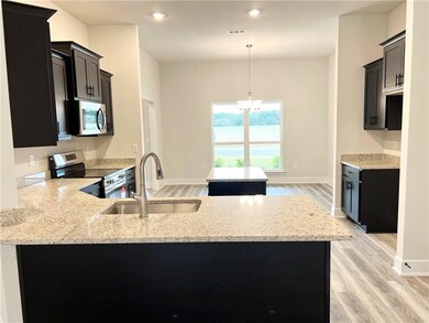 Kitchen featuring stainless steel appliances, light stone counters, a center island, dark cabinetry, and pendant lighting