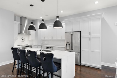 Kitchen featuring appliances with stainless steel finishes, white cabinetry, a kitchen breakfast bar, wall chimney exhaust hood, and dark wood-style floors