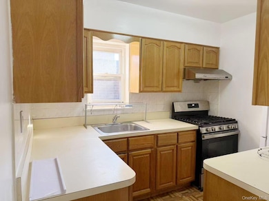 Kitchen featuring stainless steel gas stove, tasteful backsplash, light countertops, under cabinet range hood, and brown cabinetry
