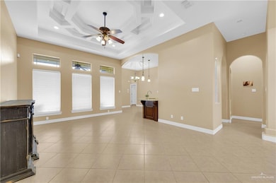 Unfurnished living room featuring arched walkways, coffered ceiling, light tile patterned flooring, a chandelier, and a ceiling fan