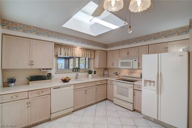 Kitchen with light tile flooring, white appliances, sink, and a skylight