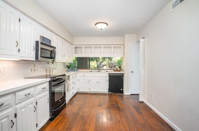 Kitchen with black appliances, light countertops, white cabinetry, and dark wood-type flooring