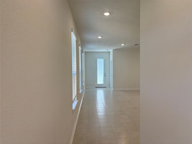 Bright hallway with tiled flooring and recessed lighting, featuring large windows and a glass door leading outside.