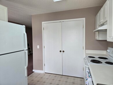 Kitchen with white appliances, under cabinet range hood, light flooring, white cabinetry, and a textured ceiling