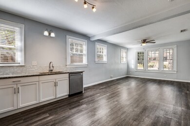 Kitchen with white cabinets, dark wood-style flooring, light stone counters, stainless steel dishwasher, and a textured ceiling