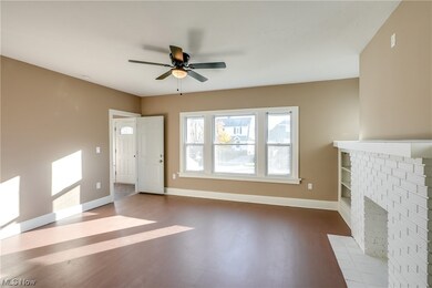 Unfurnished living room with hardwood floors, ceiling fan (2023), and a decorative brick fireplace. New windows and doors! (2023)