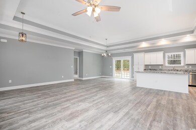 Unfurnished living room featuring ceiling fan, light wood-type flooring, ornamental molding, and a tray ceiling